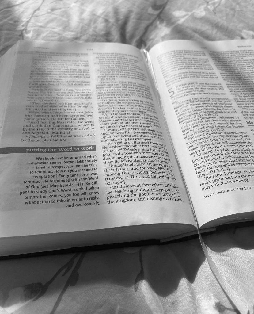 Black and White image with Bible open up on bed and afternoon sun rays shining on pages