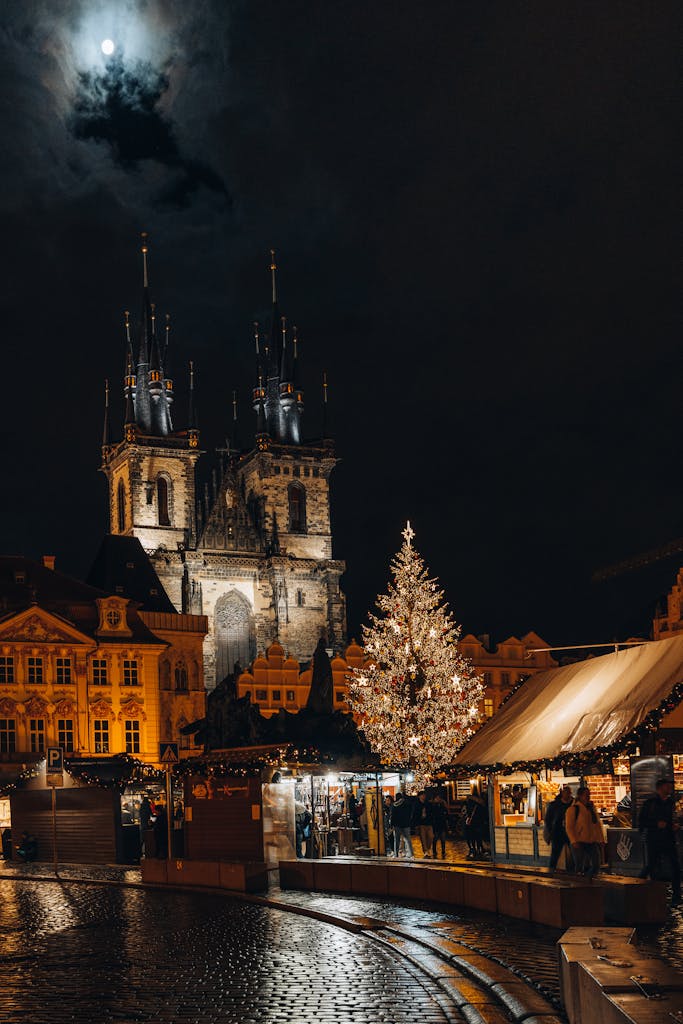 Magical Christmas market in Prague with illuminated tree and historic church under a full moon.