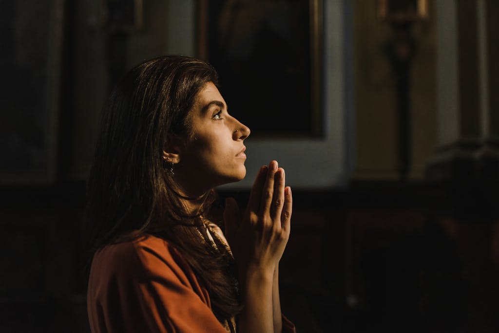 Side profile of a woman praying indoors with hands together, creating a serene and religious ambiance.