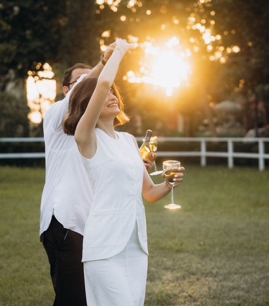 A cheerful couple dances outdoors at sunset, enjoying wine and the warm atmosphere.
