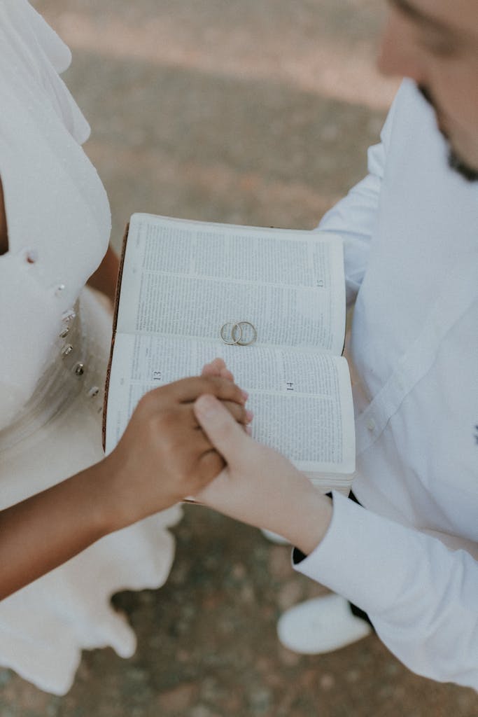 A couple holding hands over an open Bible during a wedding ceremony, symbolizing unity and faith.