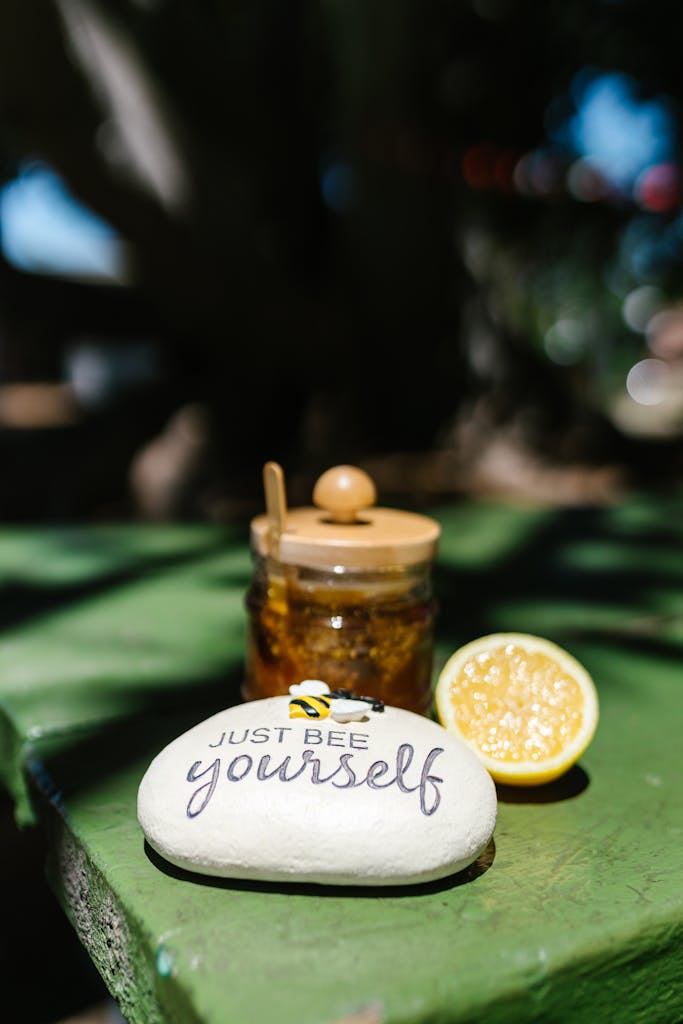 A jar of honey, lemon half, and motivational rock on an outdoor table.
