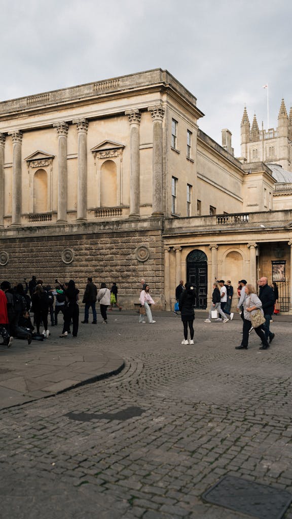 Street view in Bath with people and historic architecture, featuring Bath Abbey in the background.