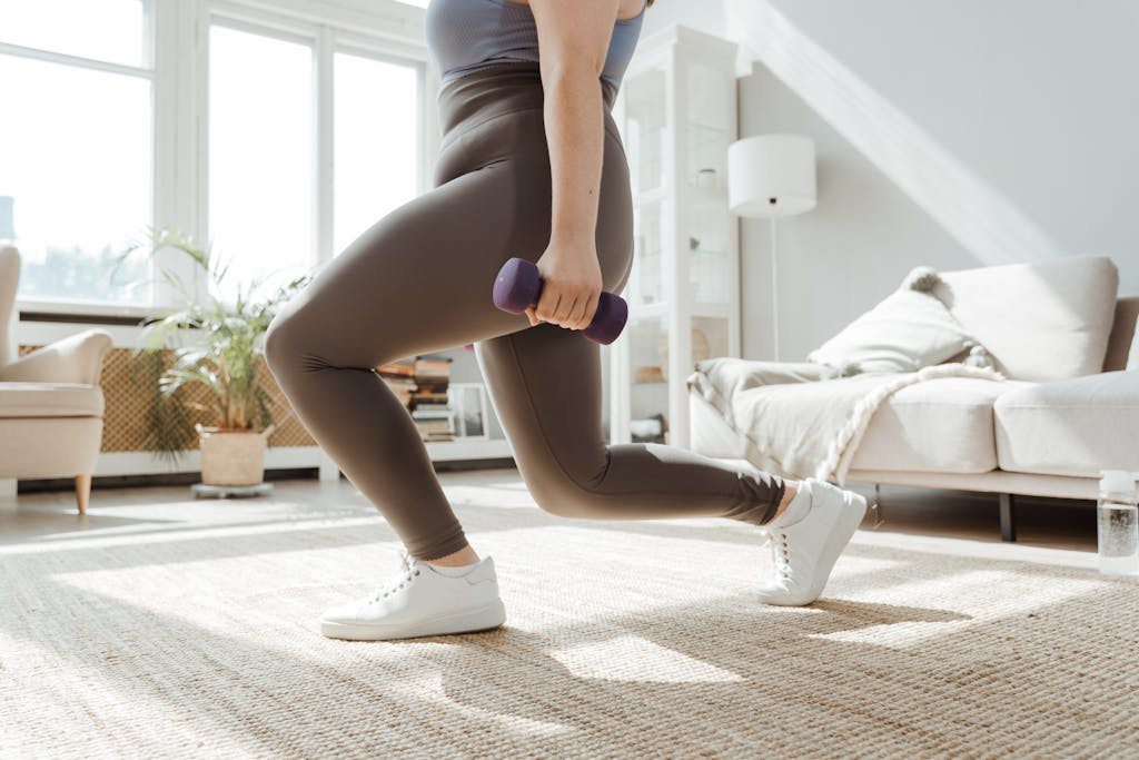A woman in active wear performs a lunges exercise with dumbbells indoors.