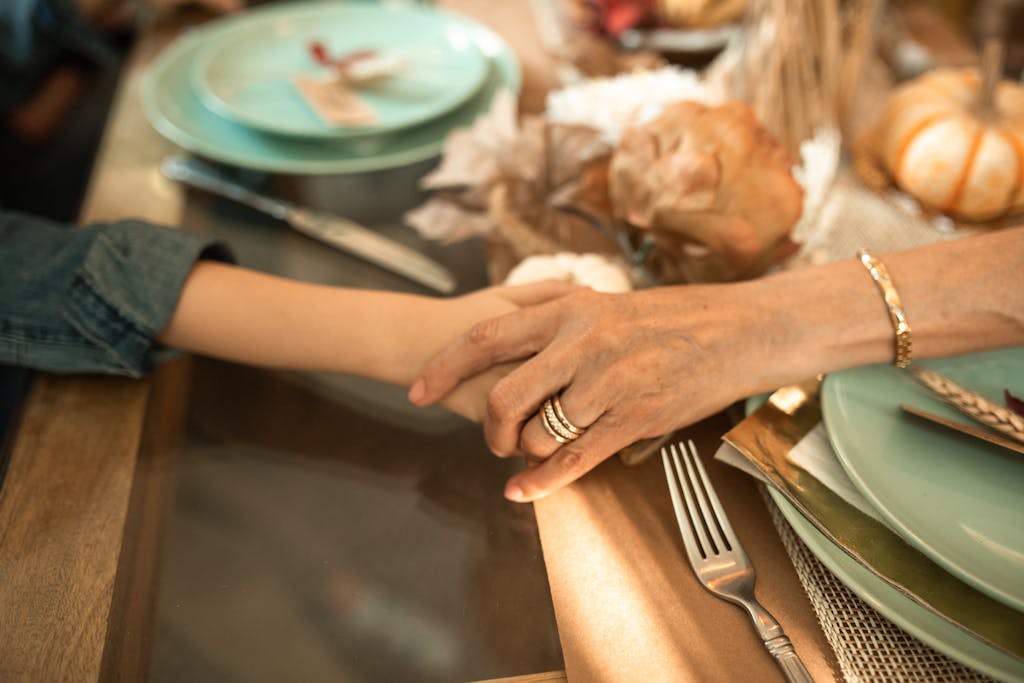 Close-up of an intergenerational handhold at a cozy Thanksgiving dinner table.