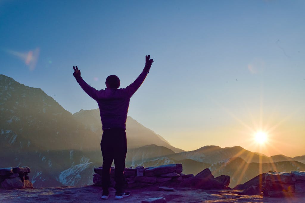 Silhouette of a man with arms raised on a mountain peak at sunset, capturing a moment of victory.
