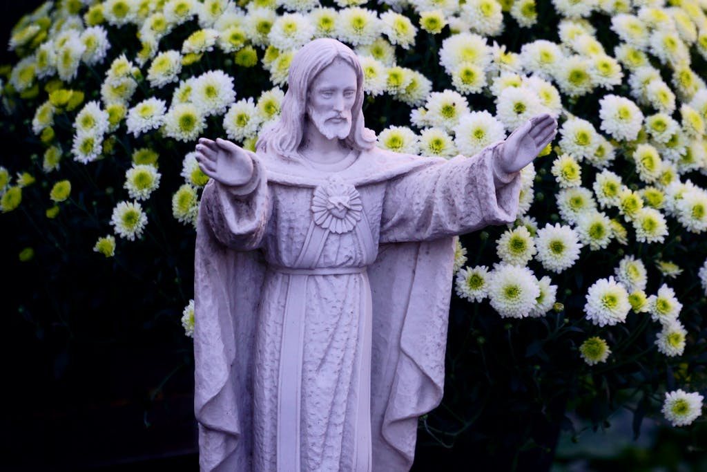 A serene Jesus Christ statue set against vibrant flowering chrysanthemums, symbolizing peace and spirituality.