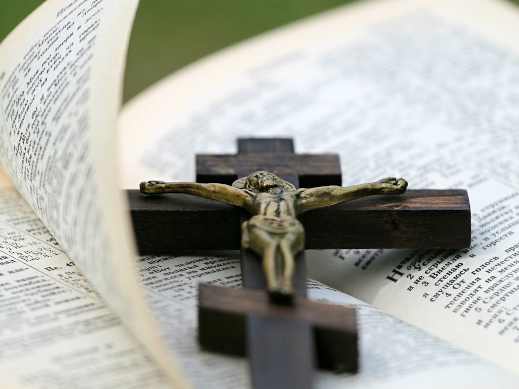 An open Bible with a brass crucifix on a dark wooden cross lying across it.