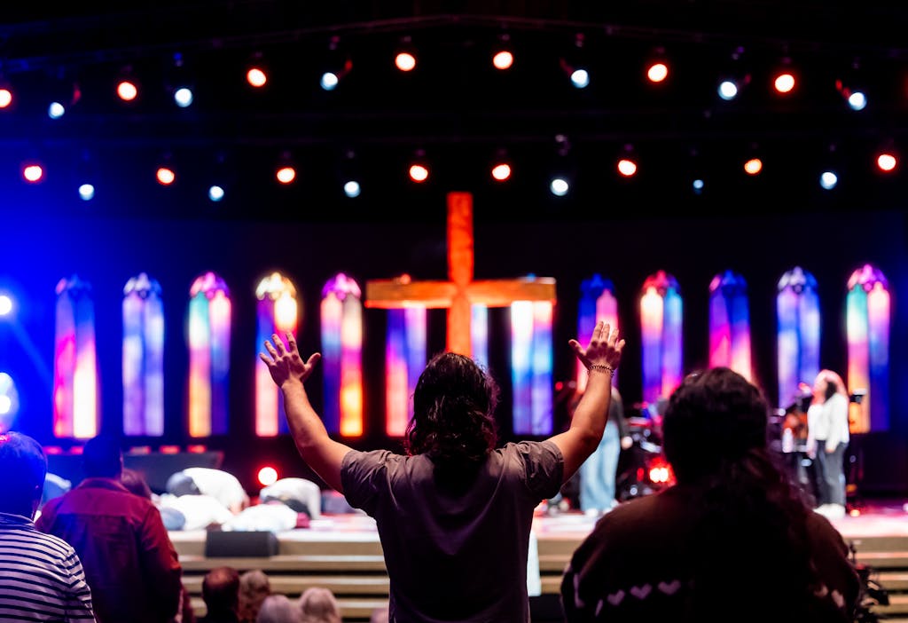 Lively church service with congregation worshipping under colorful stained-glass lighting.