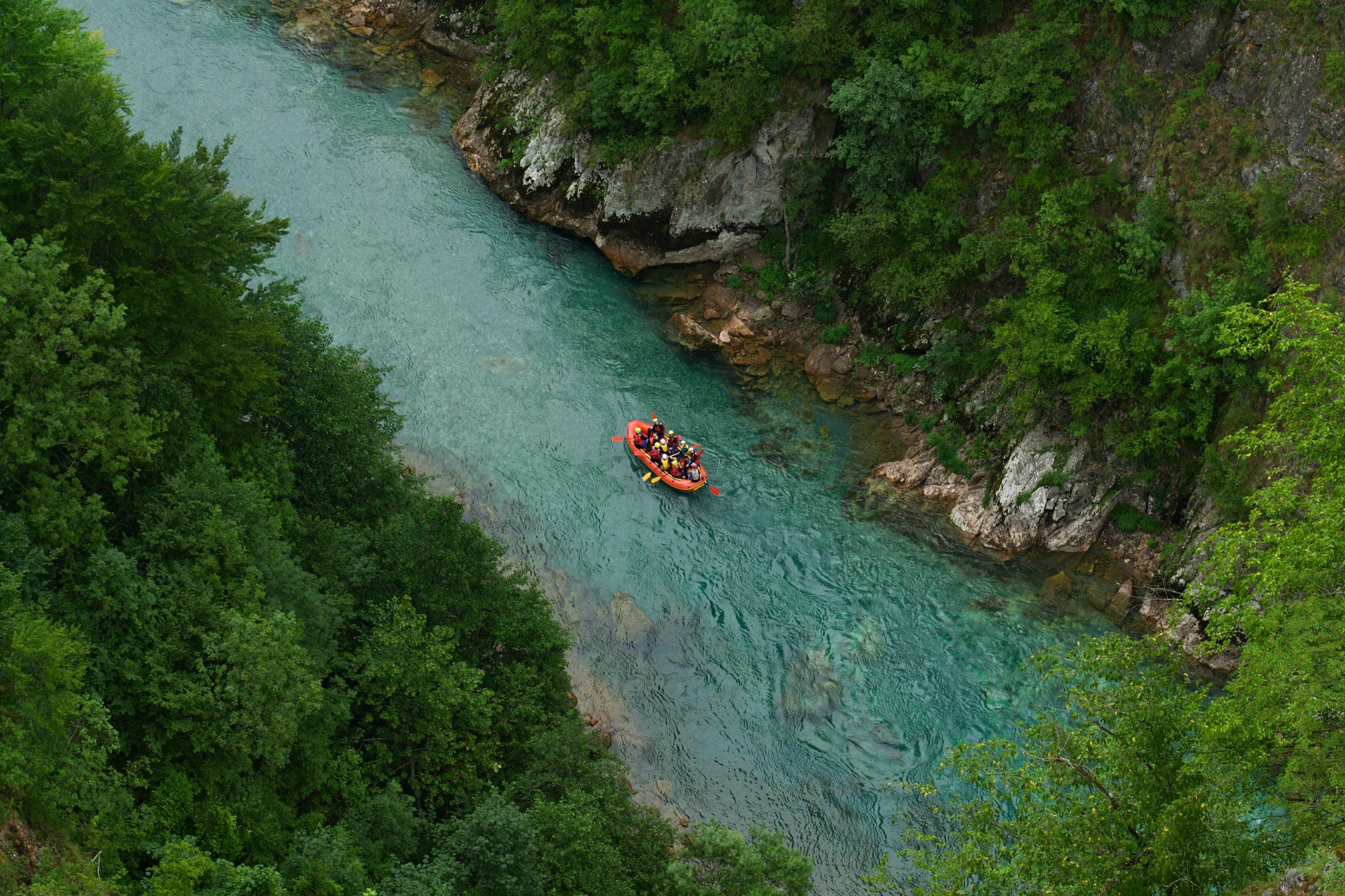 Aerial view of a group rafting down a vibrant turquoise river in Montenegro, surrounded by lush greenery.