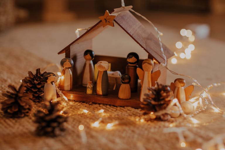 A wooden nativity scene surrounded by warm Christmas lights and pinecones.