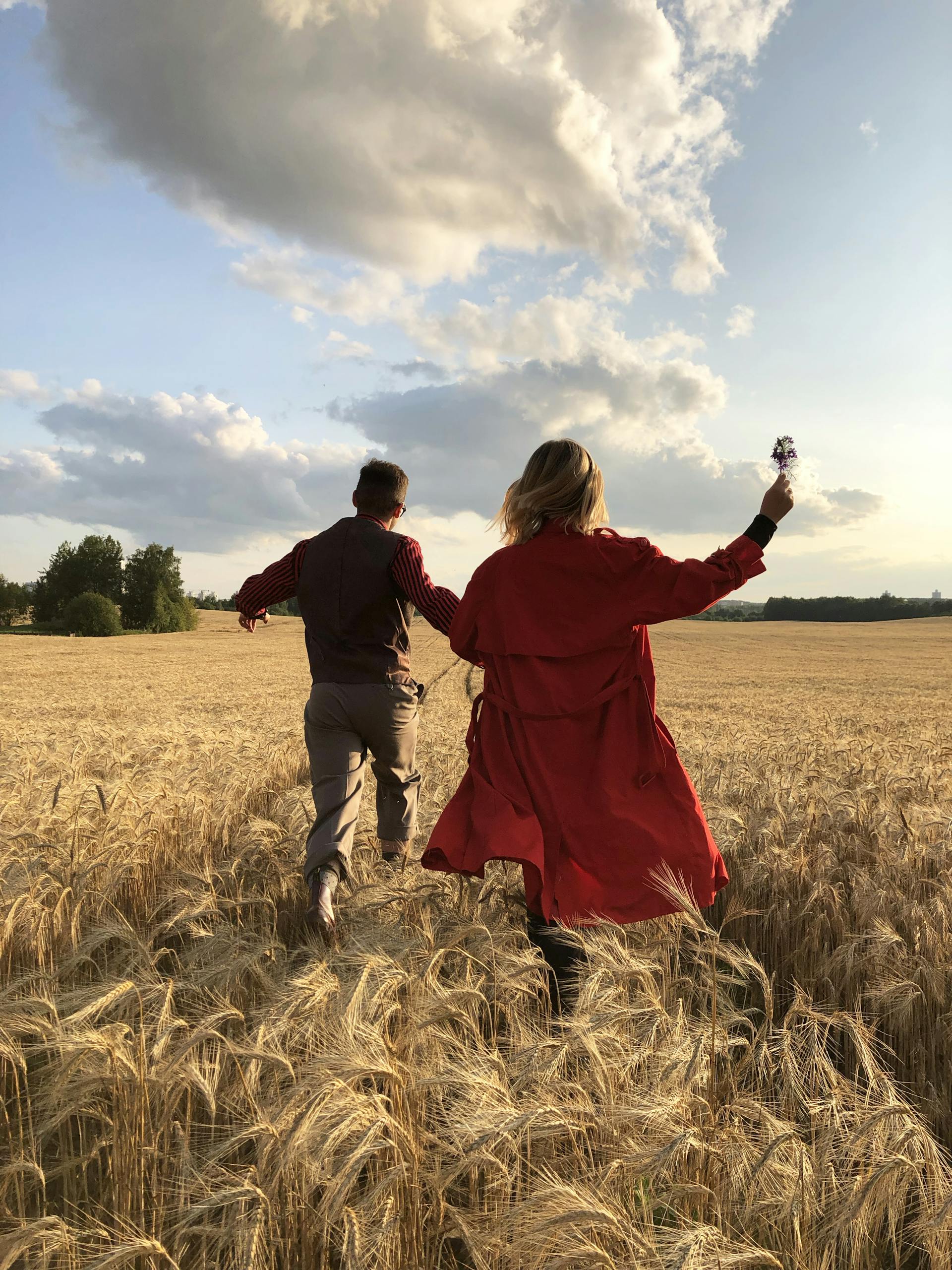 A couple joyfully running through a picturesque wheat field in the countryside during sunset.