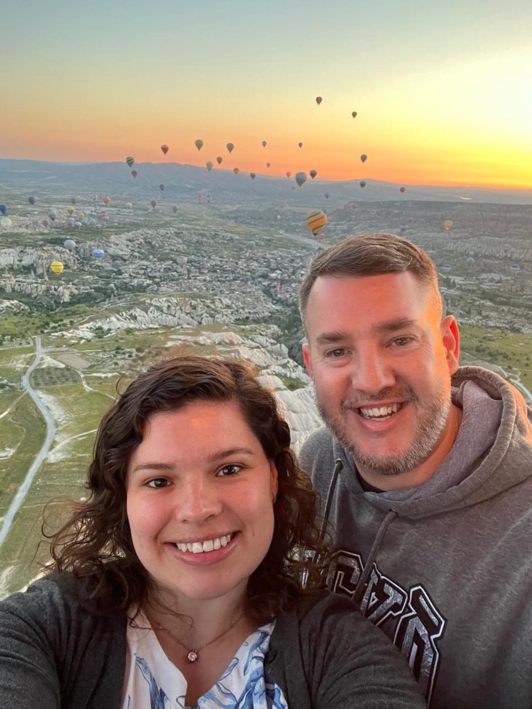 Couple in a hot air balloon in Cappadocia, Türkiye, having fun together, with a beautiful sunrise in the bakground.