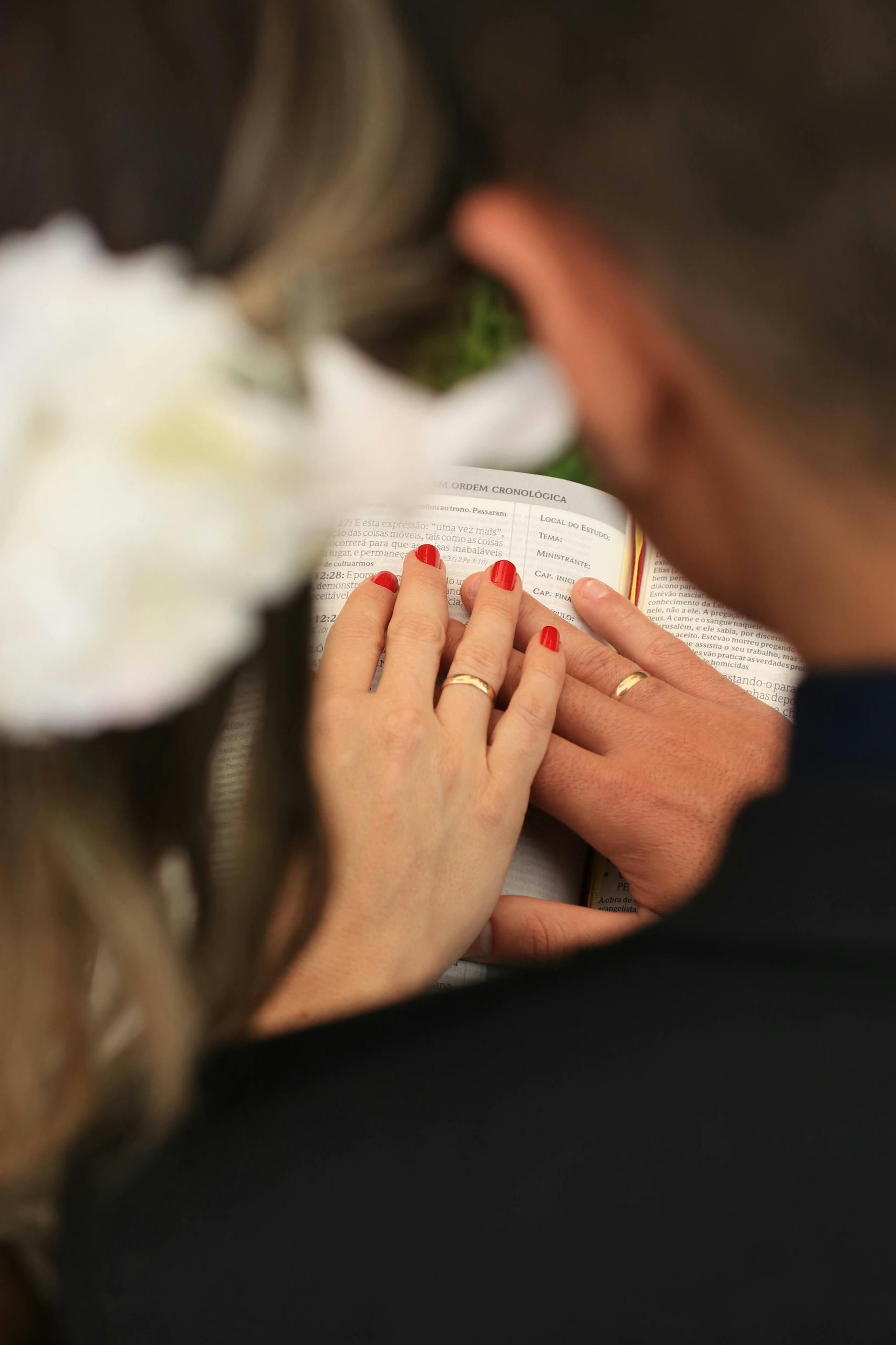 Back view of a bride and groom holding hands with wedding rings while reading the Bible, symbolizing love and commitment.