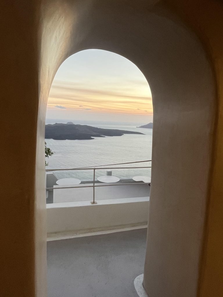 Sunset from a cliff-side restaurant in Fira, Santorini. White-washed walls bathed in light from the sun setting.