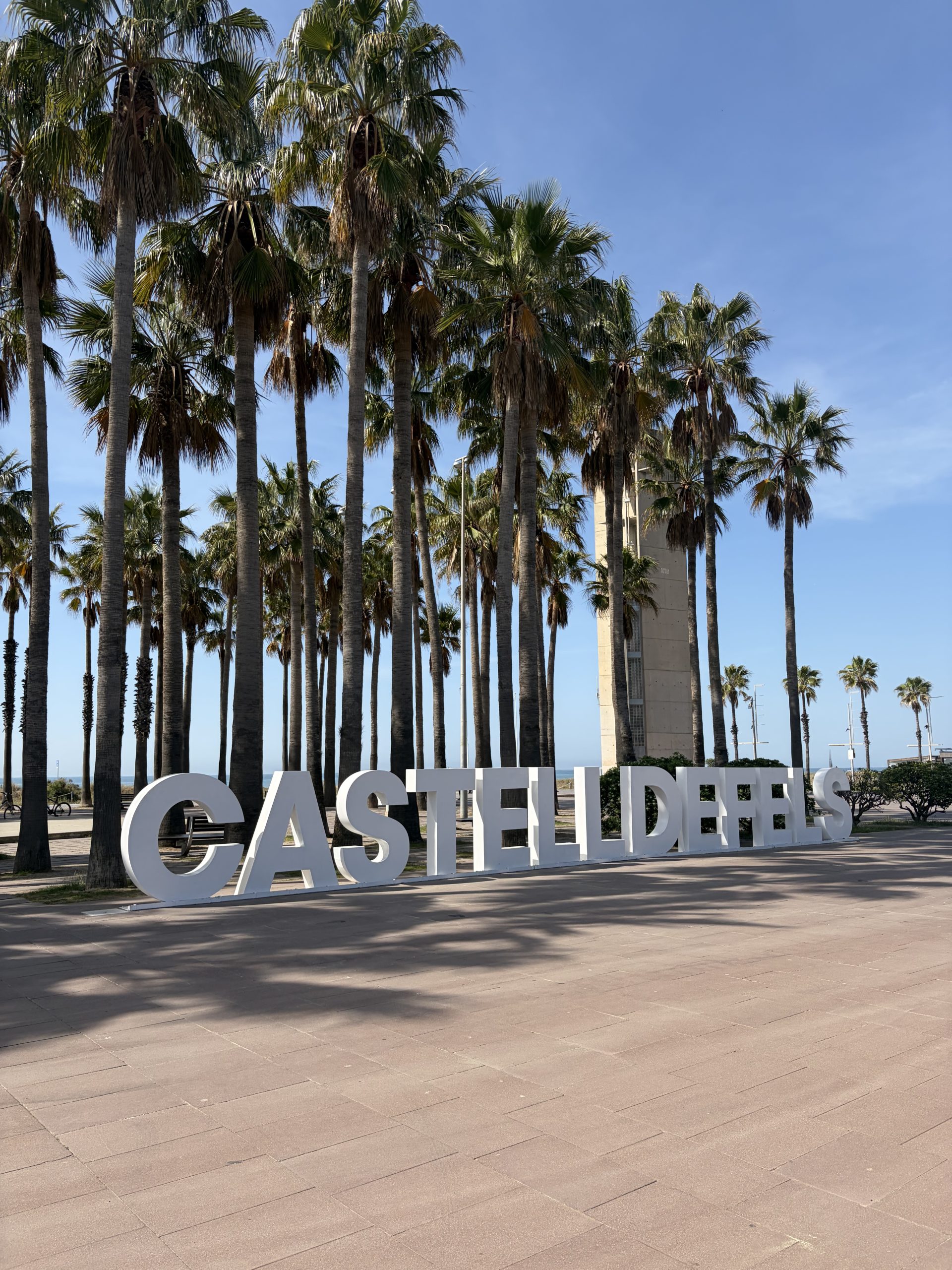Castelldefels sign in Barcelona, Spain surrounded by palm trees and blue skies.