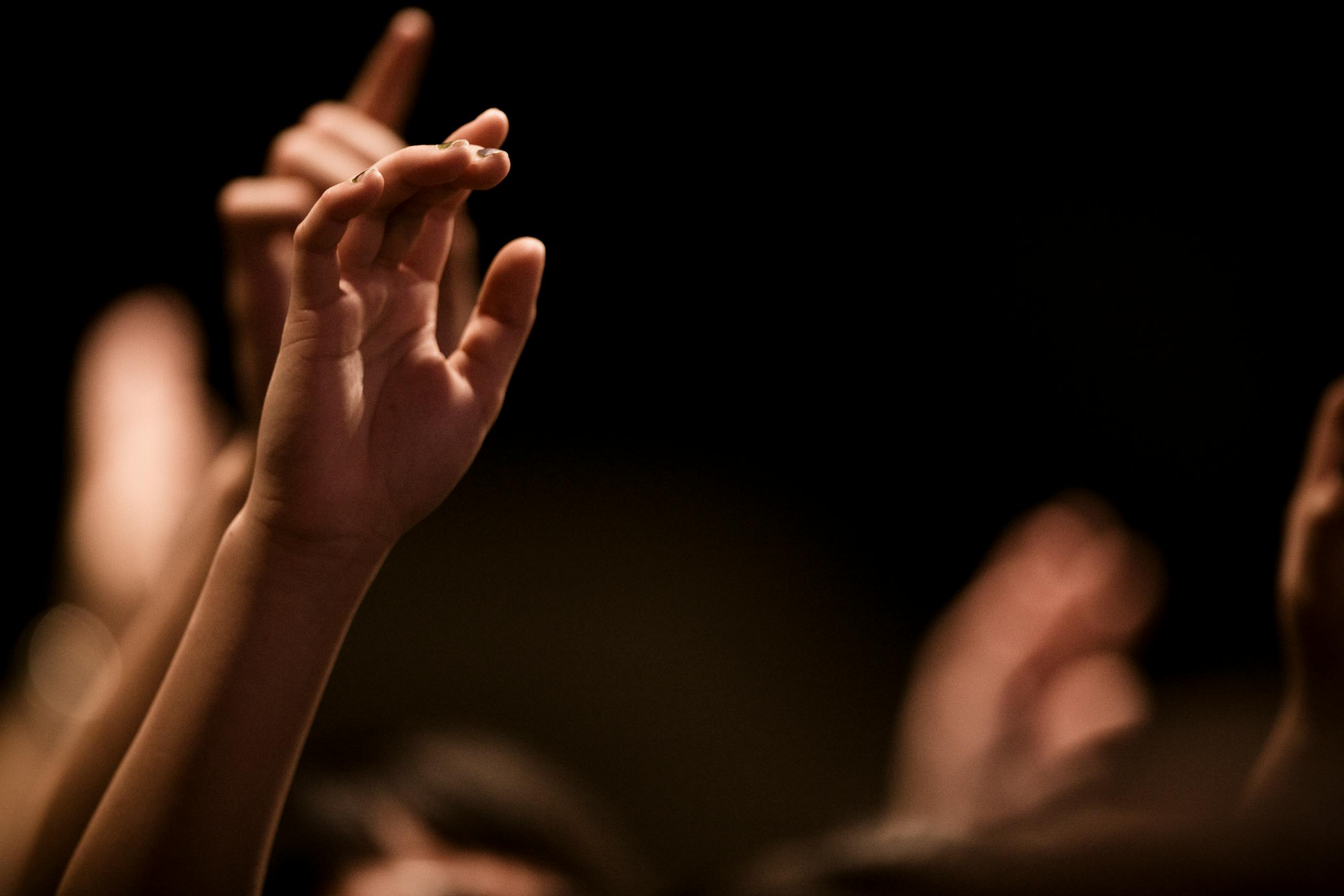 A close-up image of hands raised in worship against a blurred background.