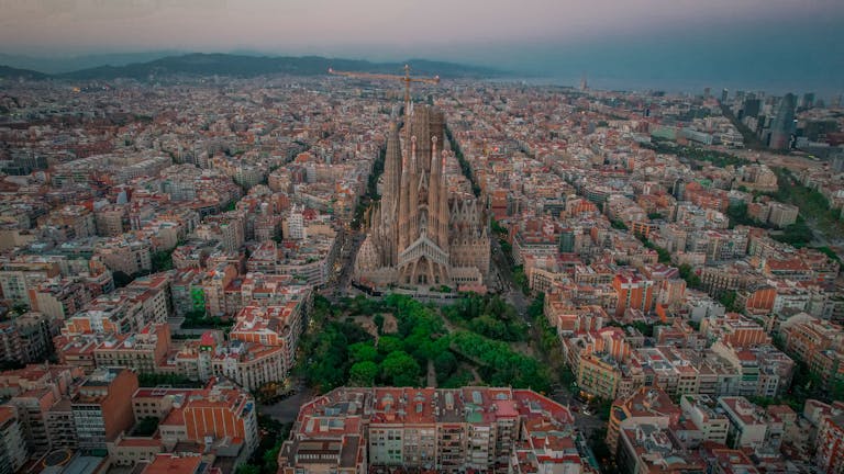 Stunning aerial photo of Sagrada Familia amidst Barcelona cityscape at twilight.