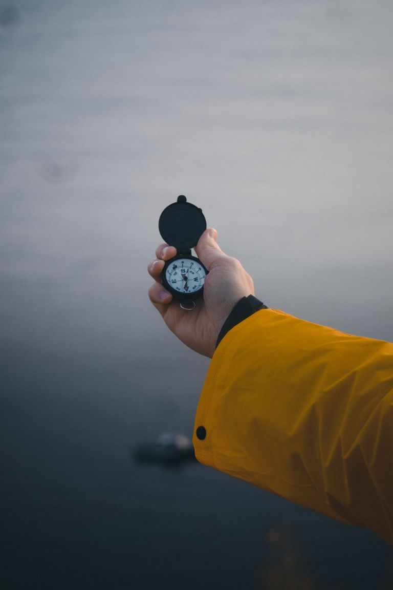 A person in a yellow jacket holds a compass in an outdoor setting, symbolizing exploration.